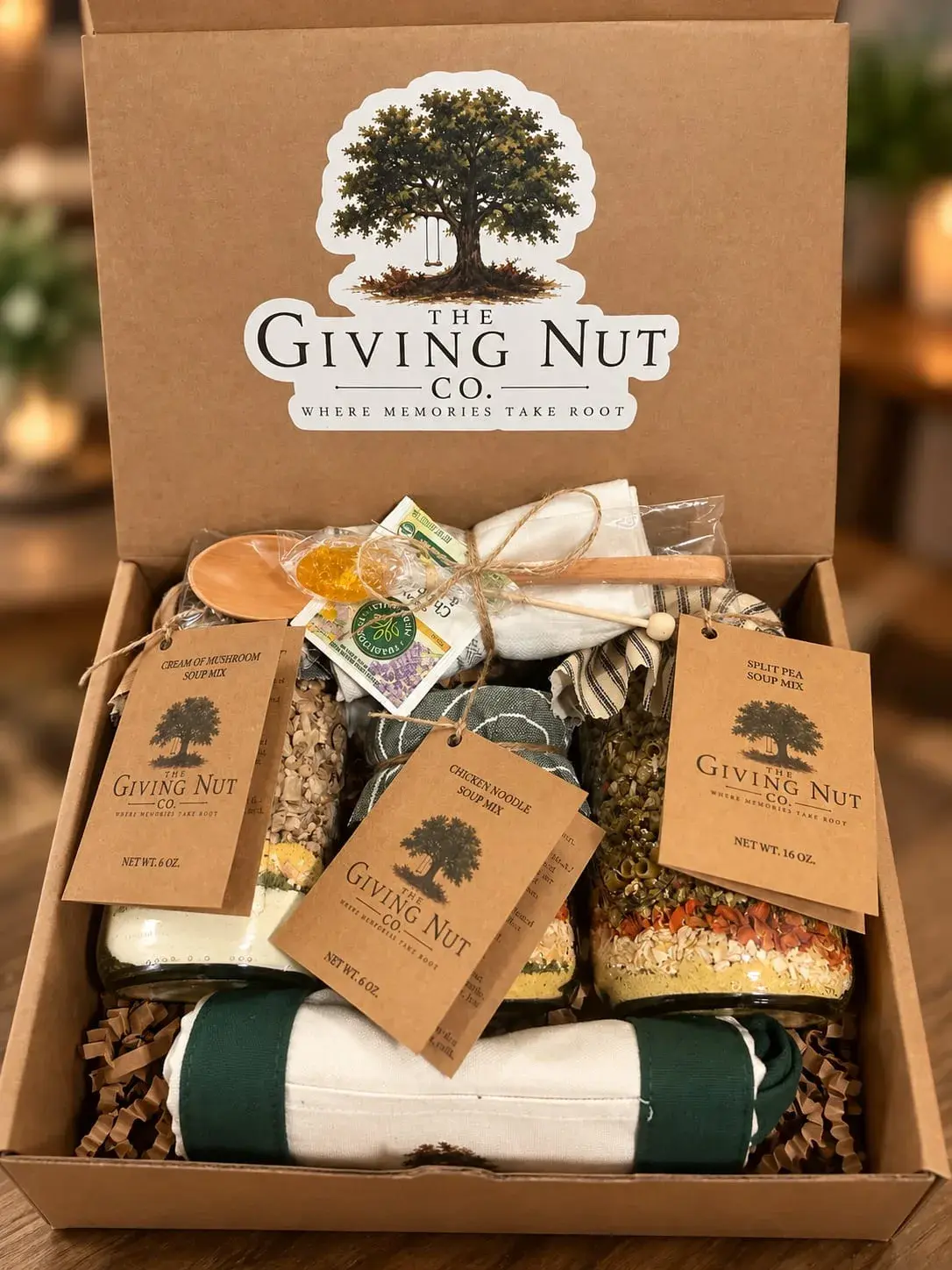 An open Giving Nut Co. gift box packed with soup mix jars, a wooden spoon and a rolled tea towel